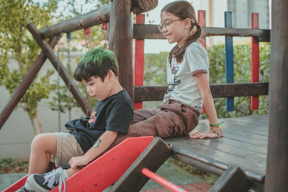 um menino de camiseta preta e uma menina de camiseta branca brincando de descer no escorregador, durante sua festa de aniversário.