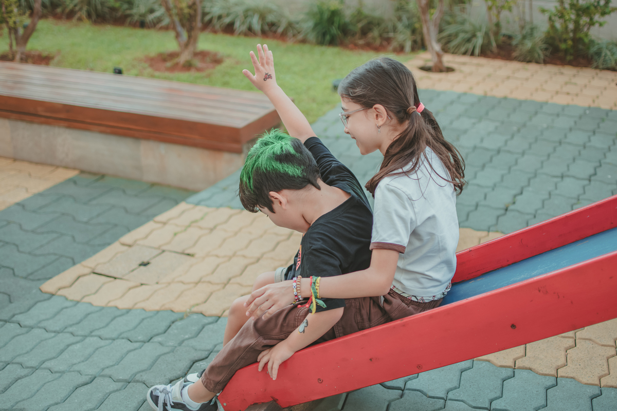 um menino de camiseta preta e uma menina de camiseta branca brincando de descer no escorregador, durante sua festa de aniversário.
