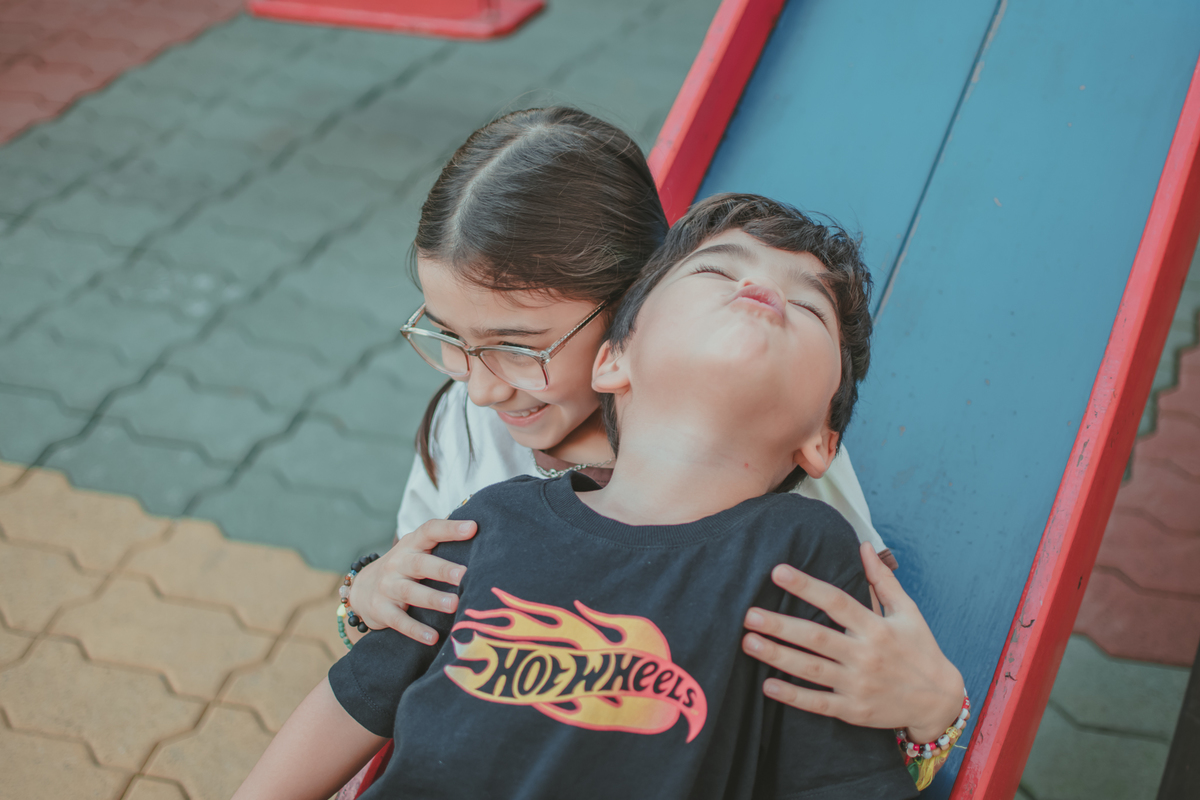 um menino de camiseta preta e uma menina de camiseta branca brincando de descer no escorregador, durante sua festa de aniversário.