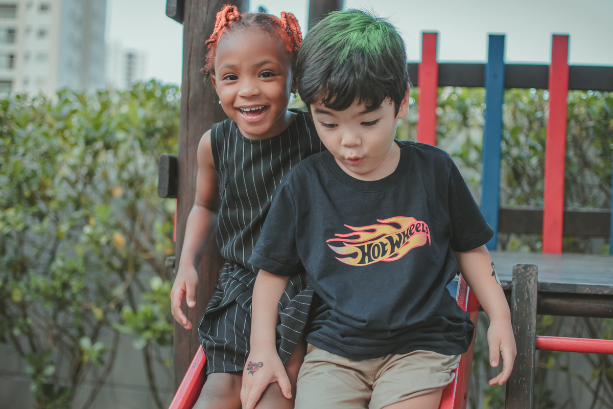 Um menino de camiseta preta e uma menina de vestido preto, brincando de escorregador durante festa de aniversário.