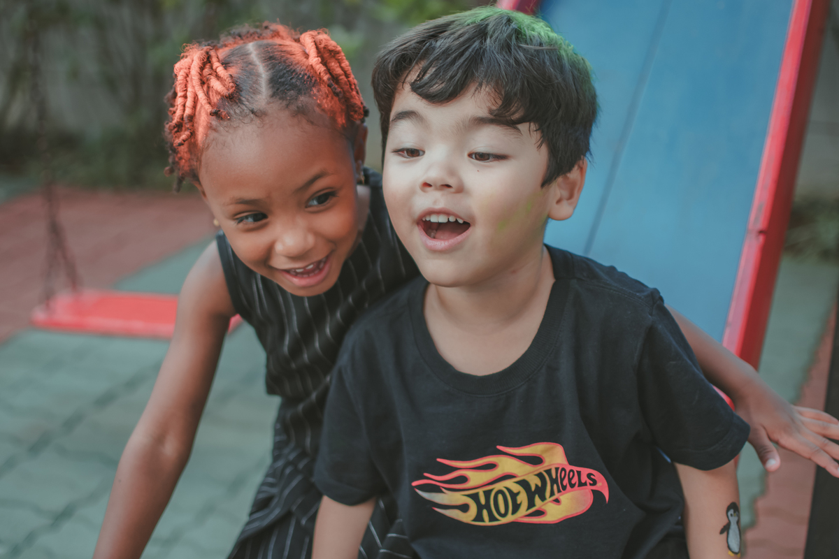 Um menino de camiseta preta e uma menina de vestido preto, brincando de escorregador durante festa de aniversário.