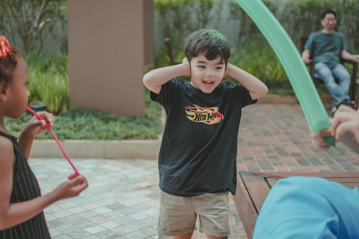 Um menino observando bexigas estourar, durante brincadeira em sua festa de aniversário.
