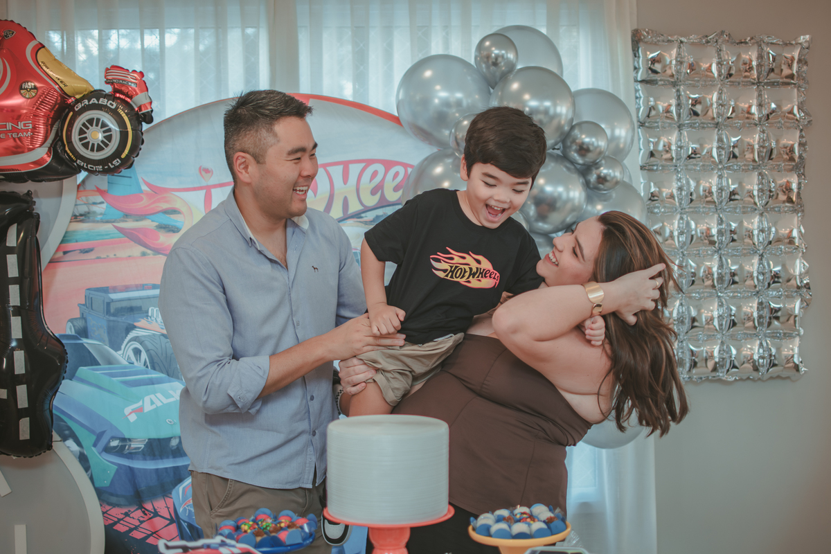 Uma familia brincando com um menino de 4 anos em seu aniversário em casa, com tema Hot Wheels.