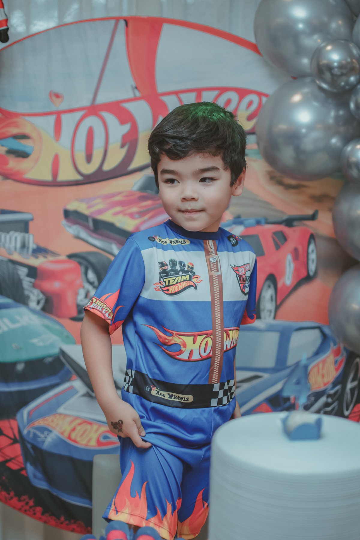 Um menino vestido de piloto de corrida da hot Wheels, durante sua festa de aniversário de 4 anos.
