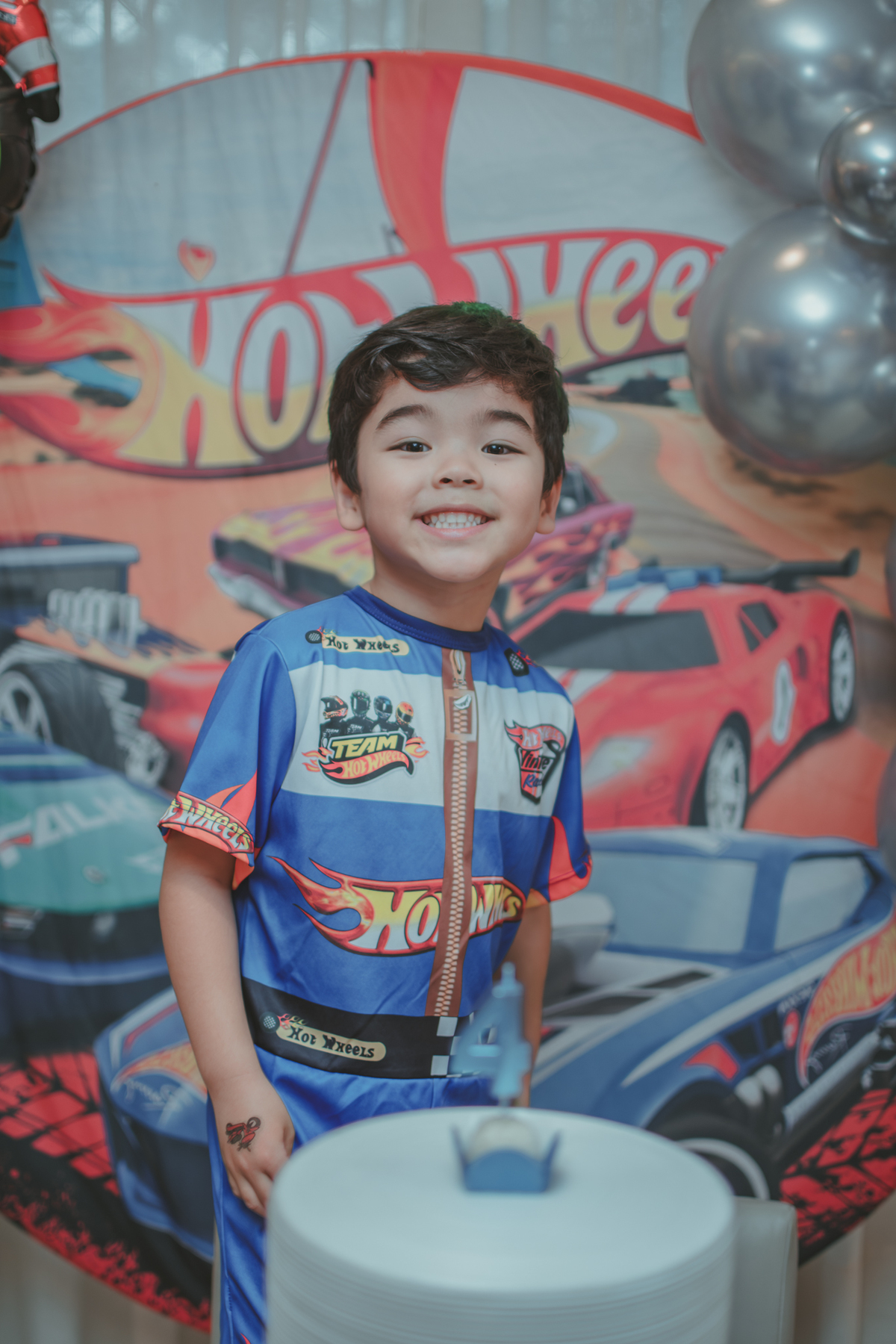 Um menino vestido de piloto de corrida da hot Wheels, durante sua festa de aniversário de 4 anos.
