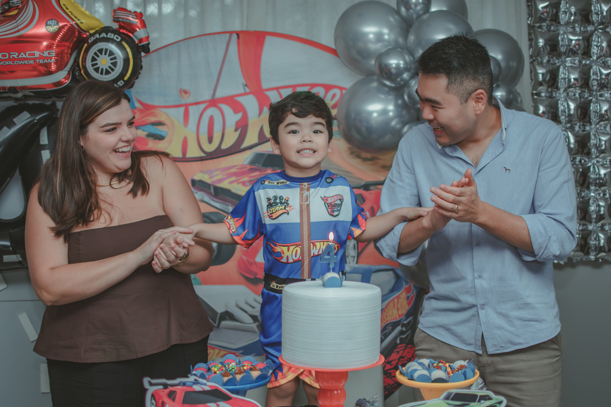 Uma familia durante o momento do parabéns na festa de aniversário de 4 anos do filho.