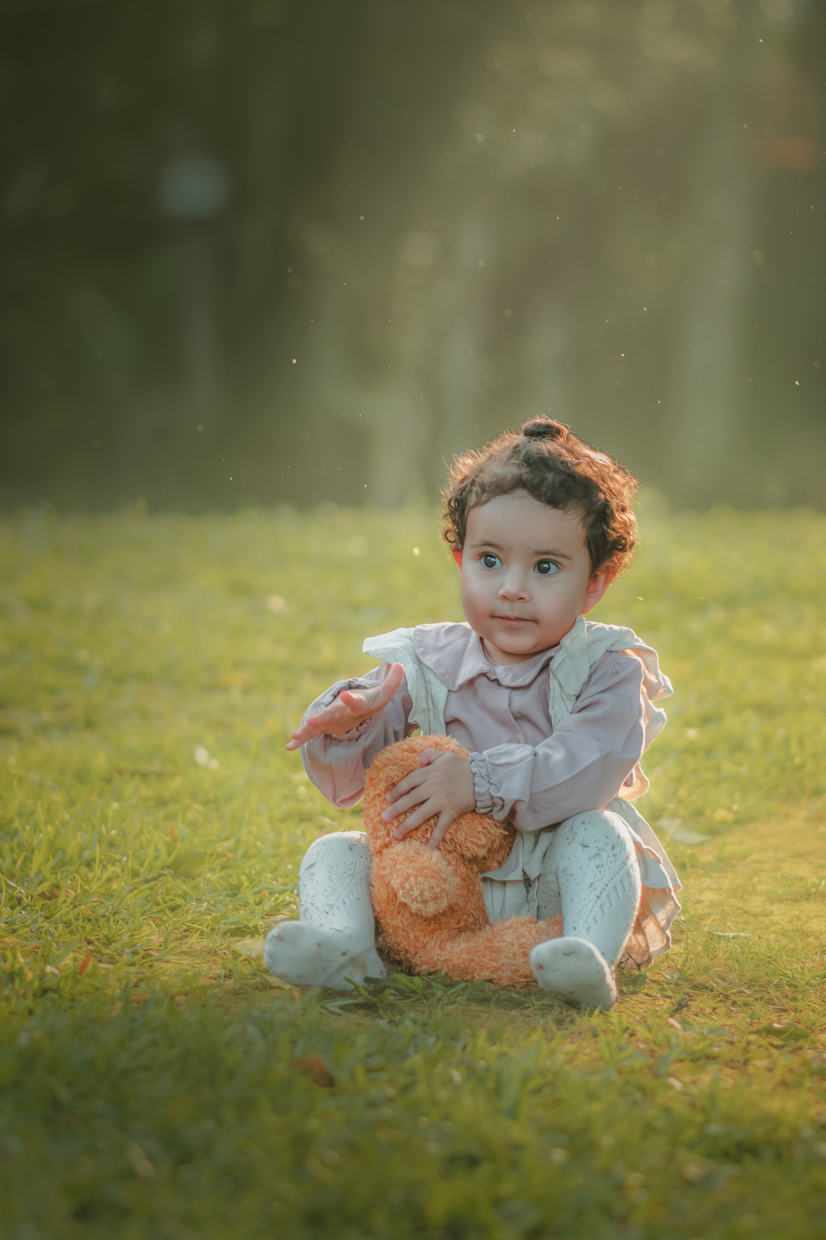 Uma bebê vestidda com roupas camponesa sentada na grama e brincando com um urso de pelúcia, durante seu ensaio de 1 ano.