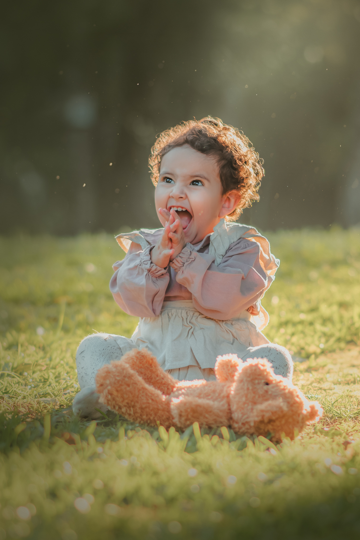 Uma bebê vestidda com roupas camponesa sentada na grama e brincando com um urso de pelúcia, durante seu ensaio de 1 ano.