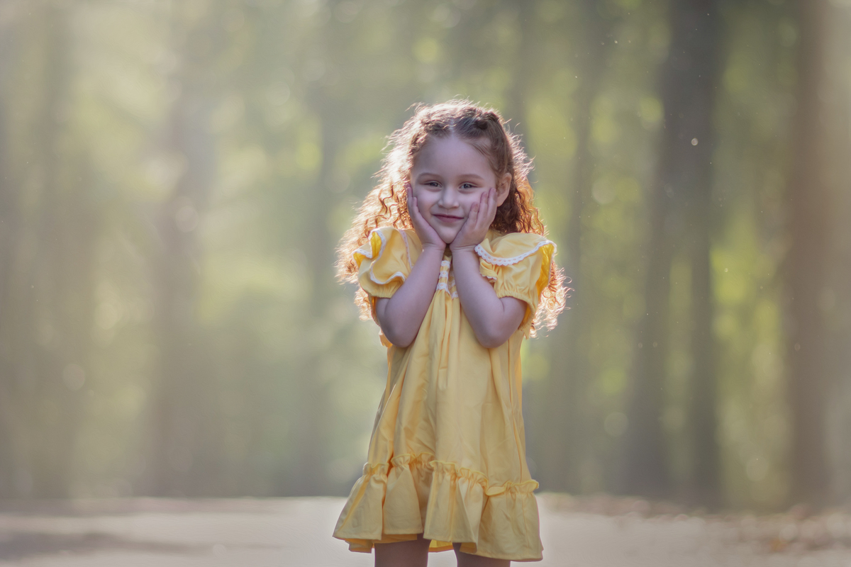 Uma menina ruiva veestida com um vestido camponês amarelo durante seu ensaio de 3 anos em um parque com muitas árvores.