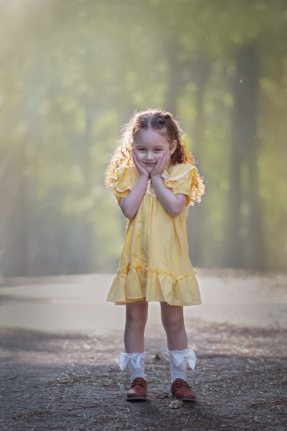 Uma menina ruiva veestida com um vestido camponês amarelo durante seu ensaio de 3 anos em um parque com muitas árvores.