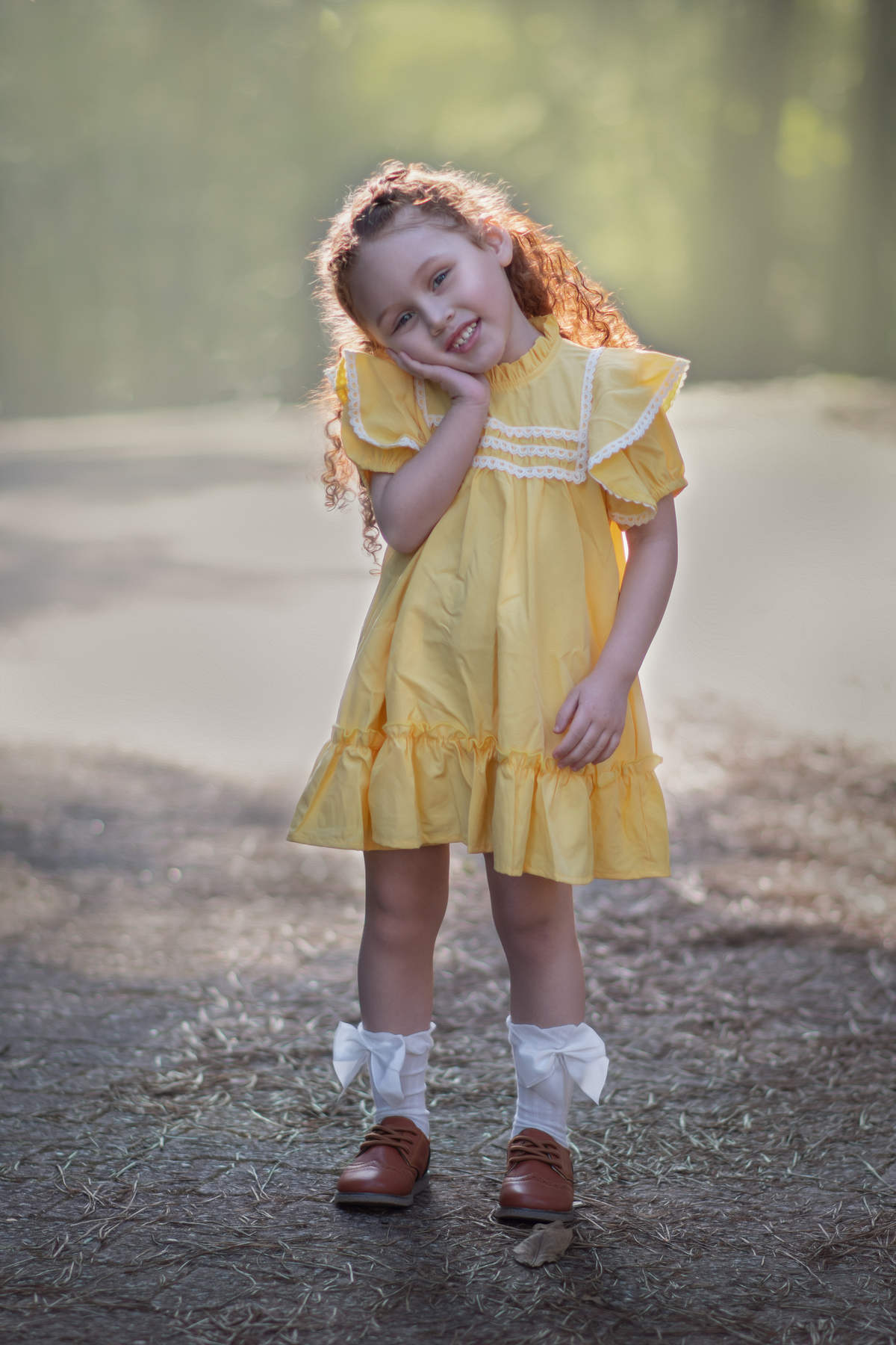 Uma menina ruiva veestida com um vestido camponês amarelo durante seu ensaio de 3 anos em um parque com muitas árvores.