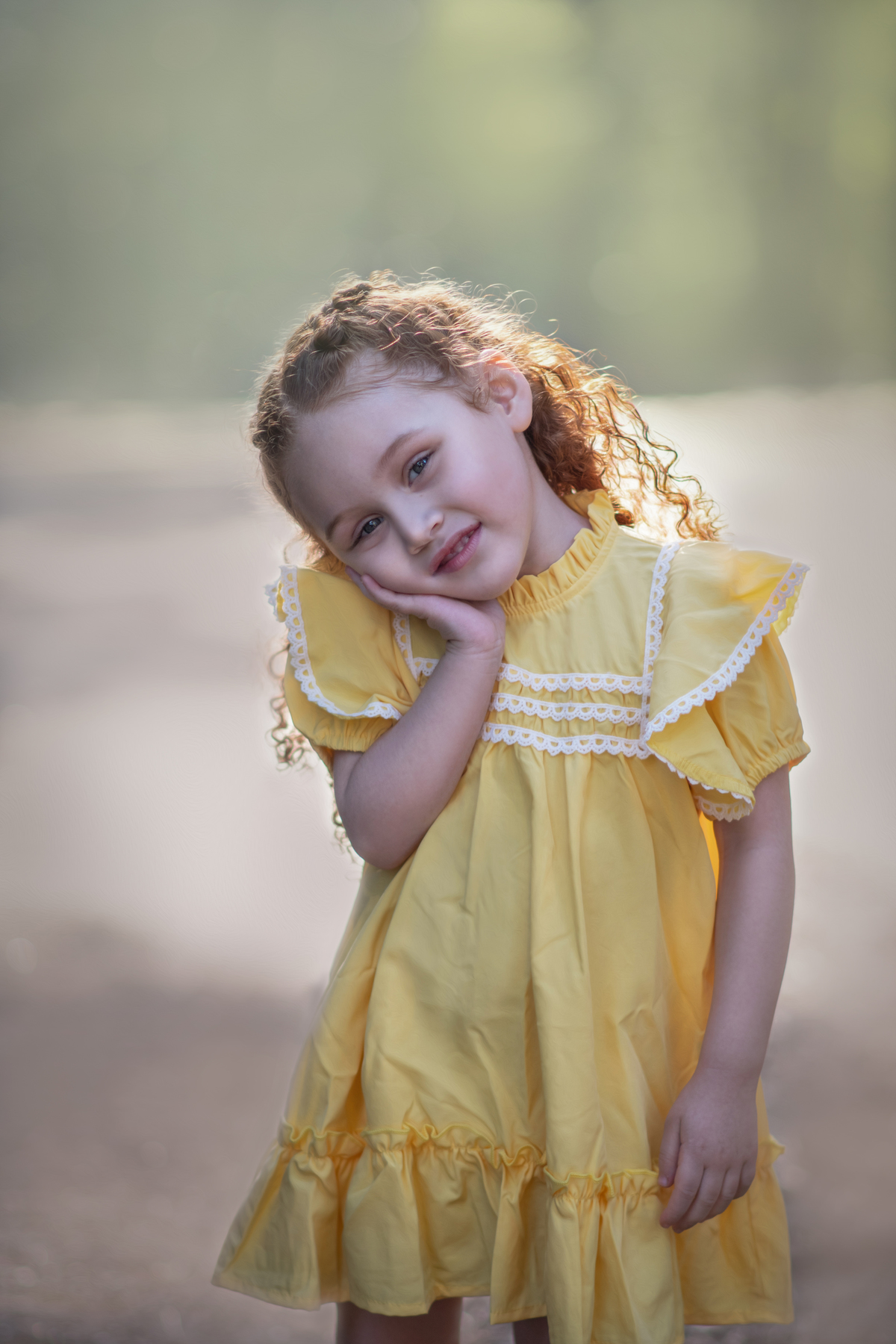Uma menina ruiva veestida com um vestido camponês amarelo durante seu ensaio de 3 anos em um parque com muitas árvores.
