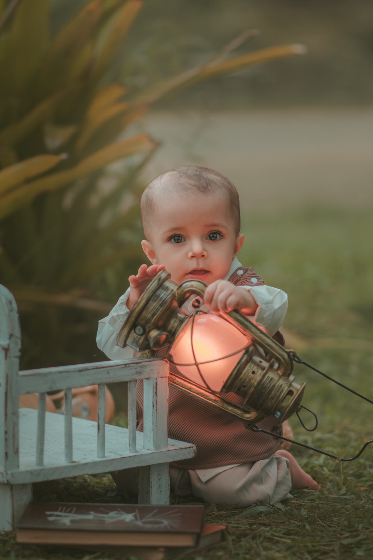 Um bebê de um aninho vestido com roupas vintage, um camisa e colete marrom, sentado em um banquinho brincando com uma arandela. Durante um ensaio fotográfico externo.