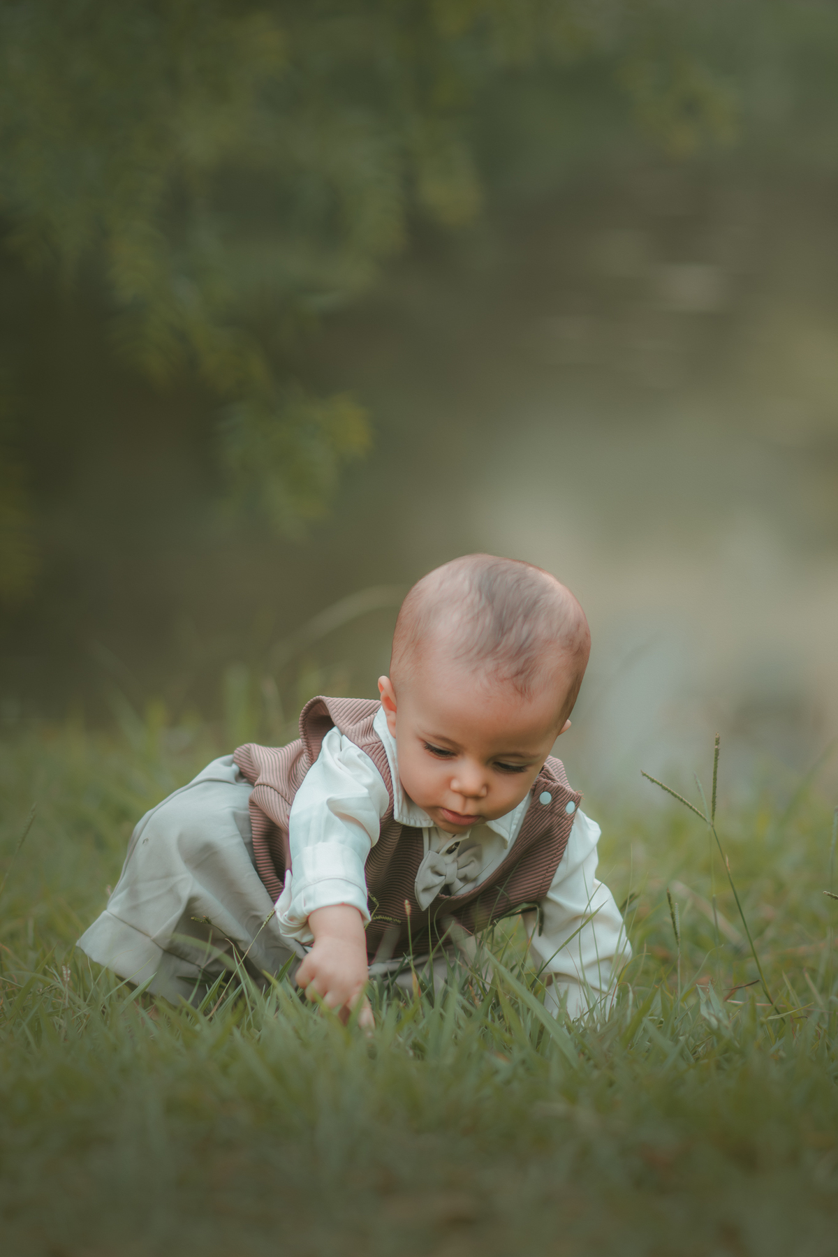 Um bebê brincando na grama usando roupas vintage, durante seu ensaio de 1 ano.