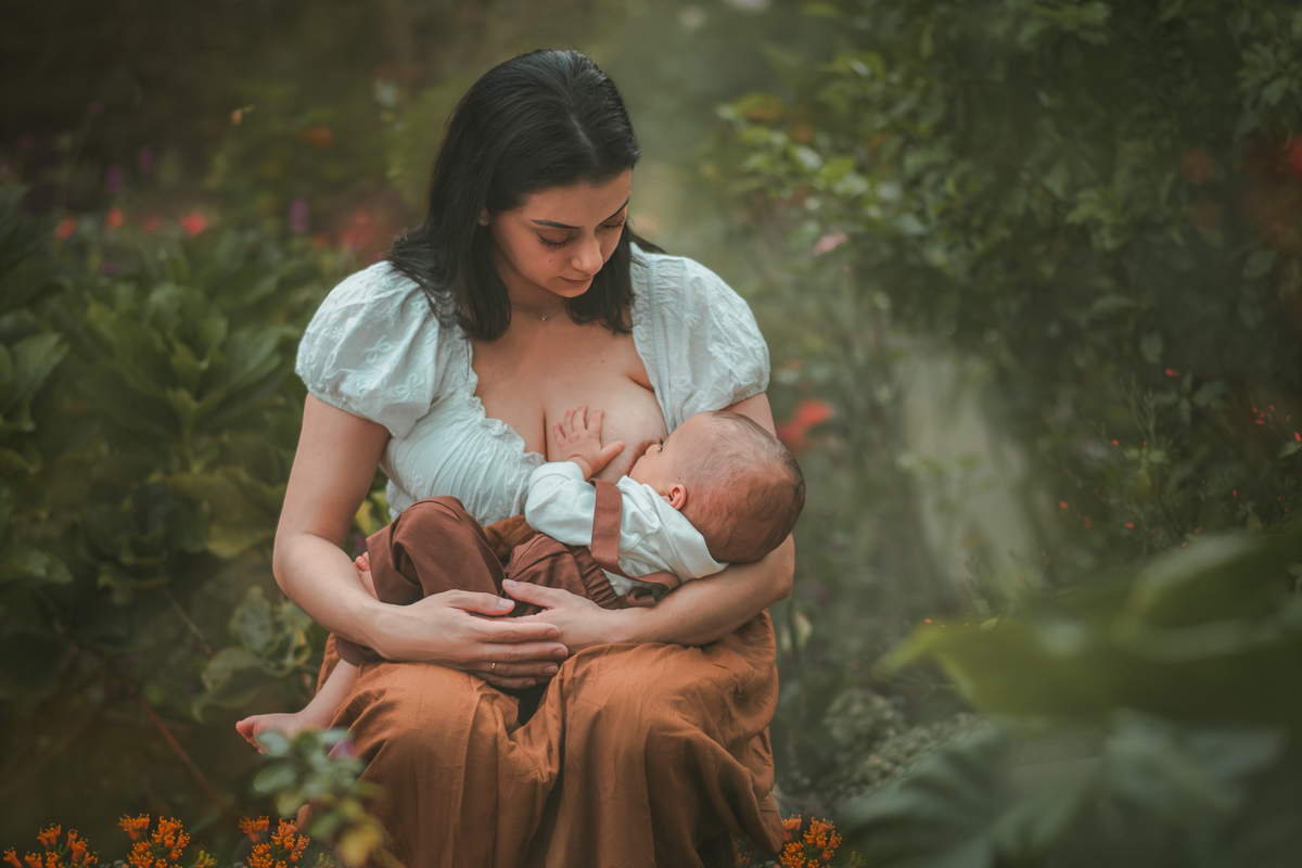 Uma mãe amamentando seu bebê em meio a natureza, durante o ensaio fotográfico de 1 ano.
