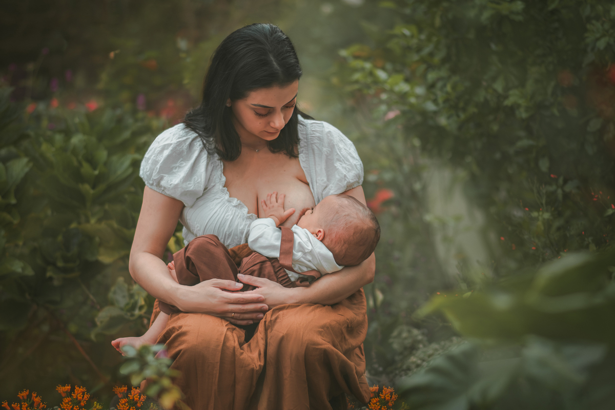 Uma mãe amamentando seu bebê em meio a natureza, durante o ensaio fotográfico de 1 ano.