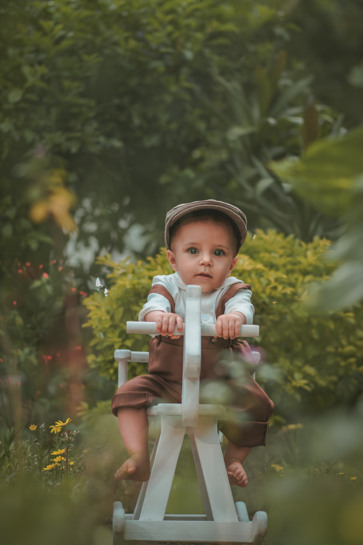 Um bebê vestido com roupas vintage, uma boina e brincando em uma cavalinho de madeira durante seu ensaio fotográfico de 1 ano.