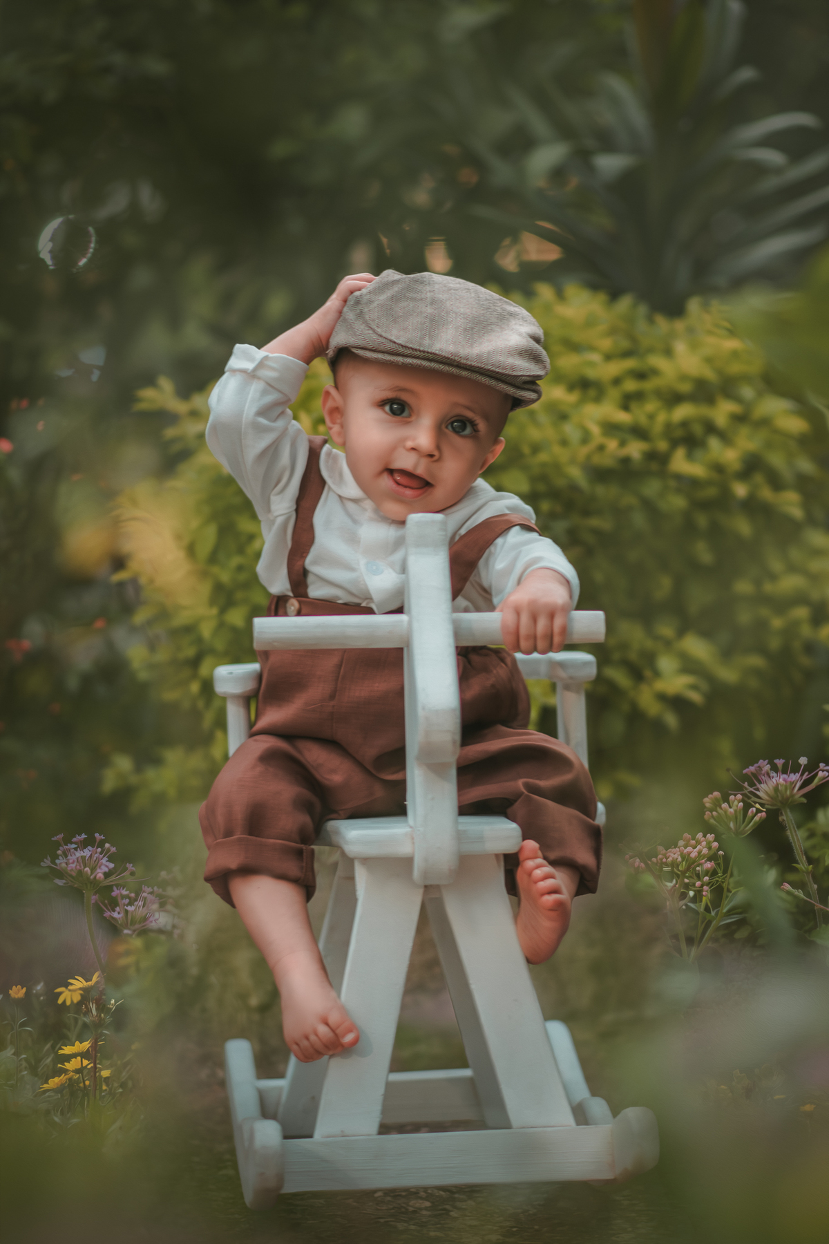 Um bebê vestido com roupas vintage, uma boina e brincando em uma cavalinho de madeira durante seu ensaio fotográfico de 1 ano.