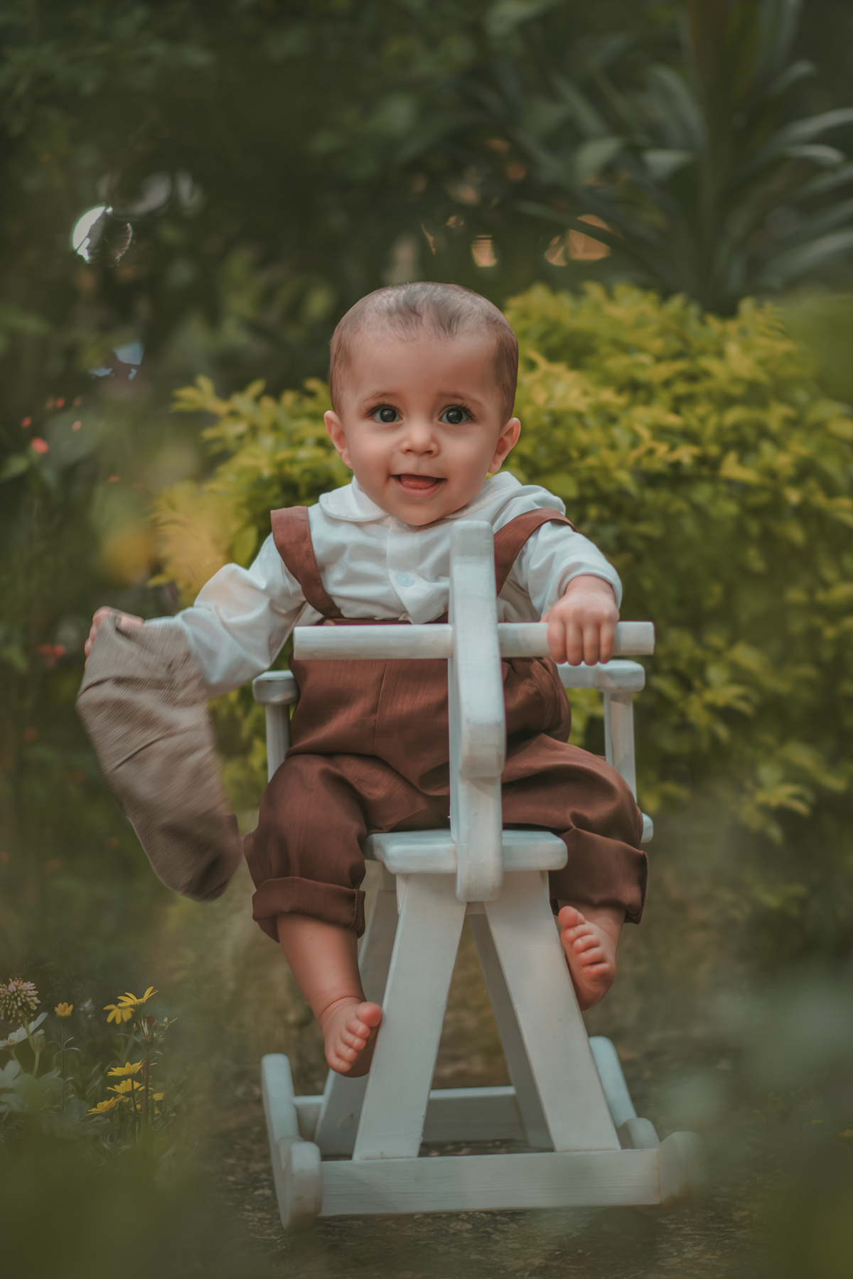 Um bebê vestido com roupas vintage, uma boina e brincando em uma cavalinho de madeira durante seu ensaio fotográfico de 1 ano.
