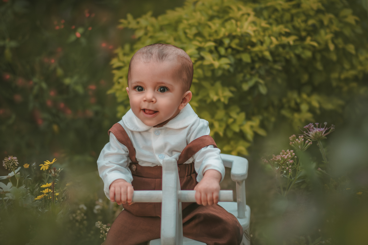 Um bebê vestido com roupas vintage, uma boina e brincando em uma cavalinho de madeira durante seu ensaio fotográfico de 1 ano.
