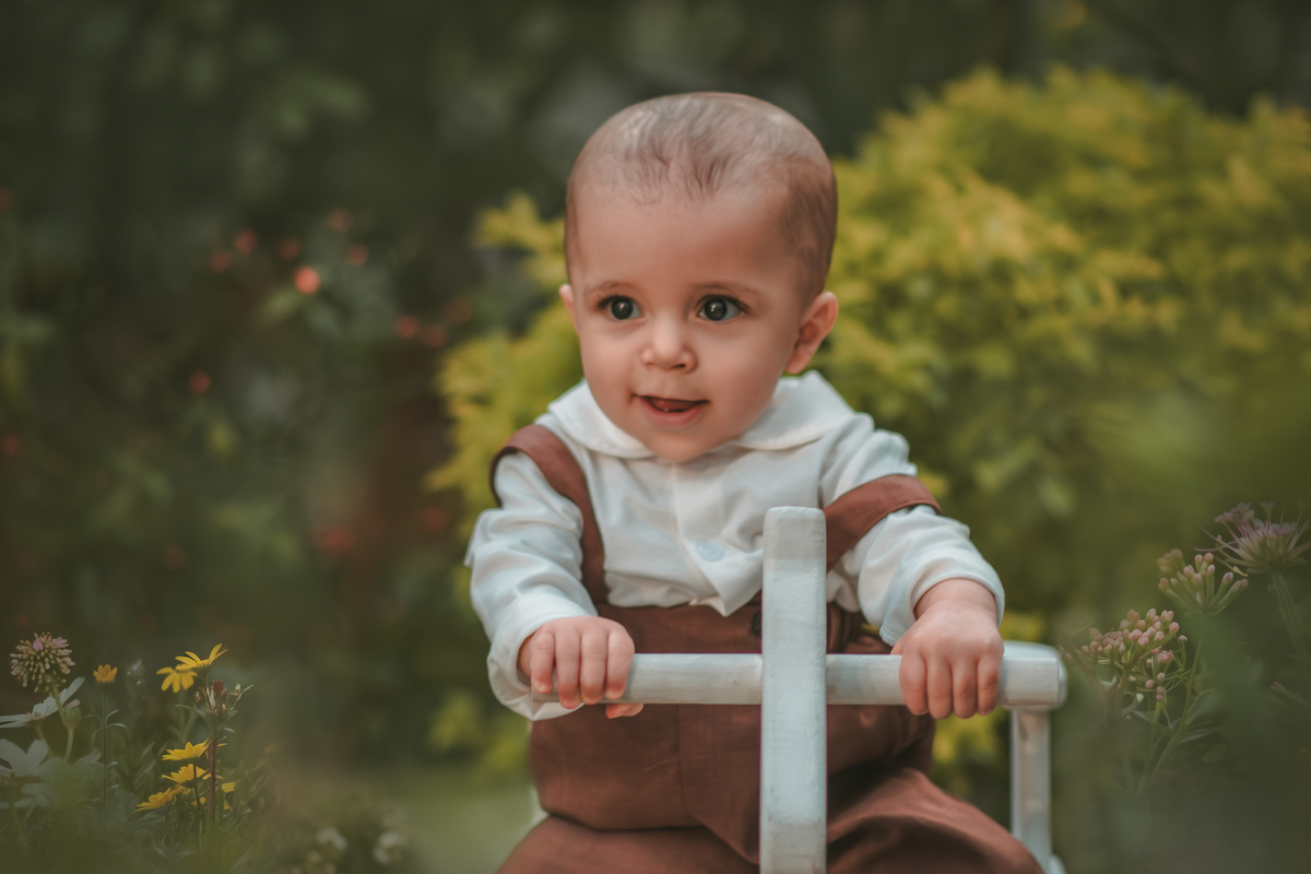 Um bebê vestido com roupas vintage, uma boina e brincando em uma cavalinho de madeira durante seu ensaio fotográfico de 1 ano.