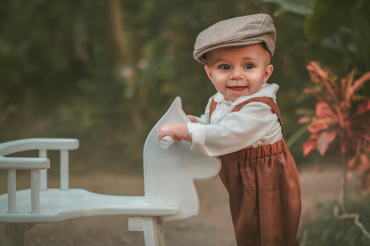 Um bebê vestido com roupas vintage, uma boina e brincando em uma cavalinho de madeira durante seu ensaio fotográfico de 1 ano.