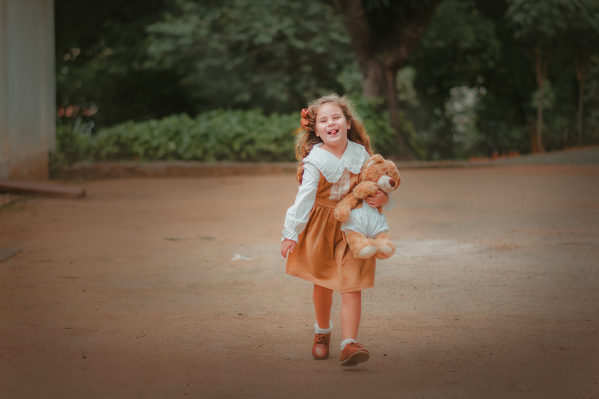 Uma menina usando roupas vintage, correndo, segurando seu ursinho de pelúcia, durante seu ensaio fotográfico.