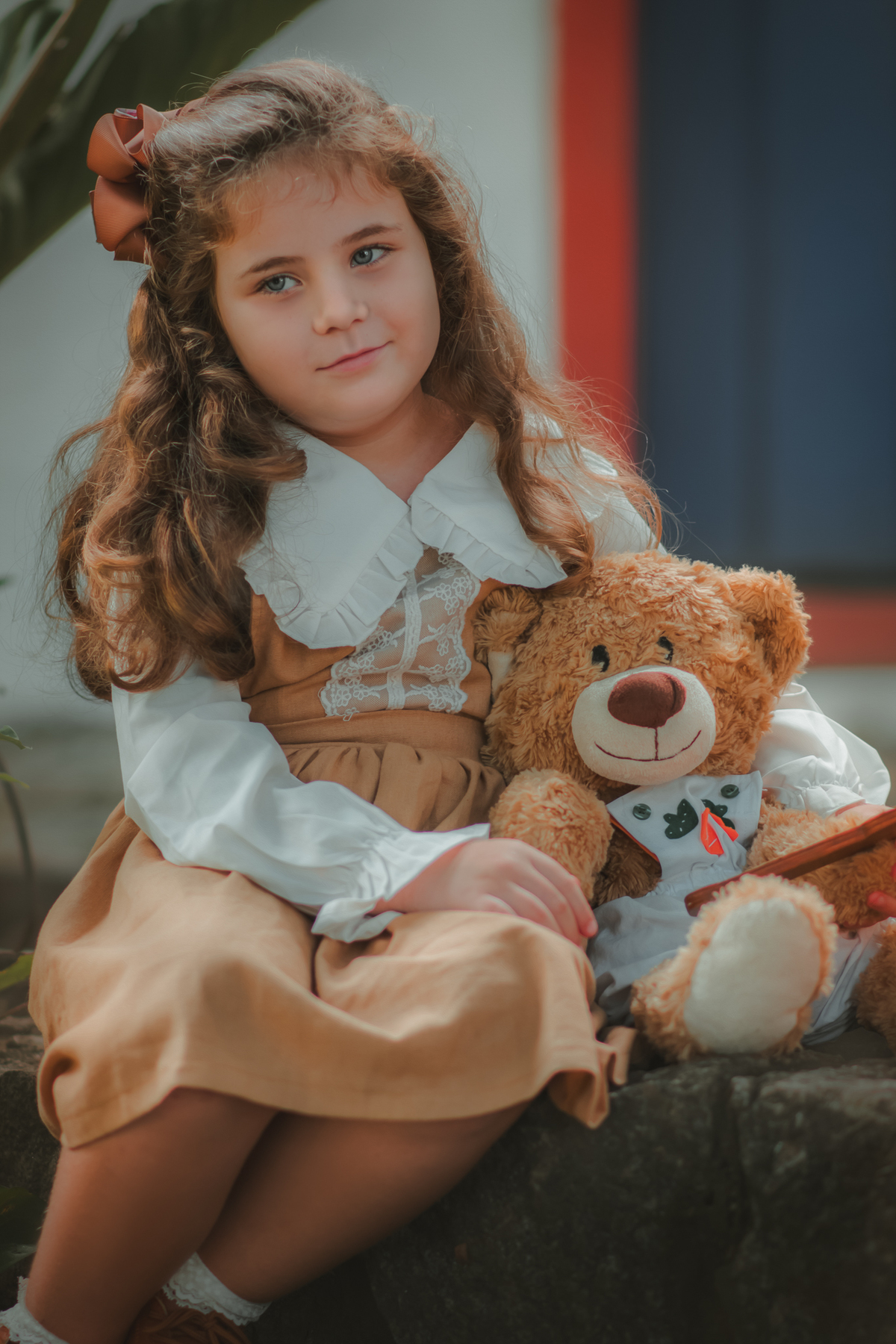 Um menina com vestido bege e blusa de gola branca, estilo camponesa vintage, segurando um espelho e ao seu lado um ursinho de pelúcia, durante seu ensaio fotográfico.