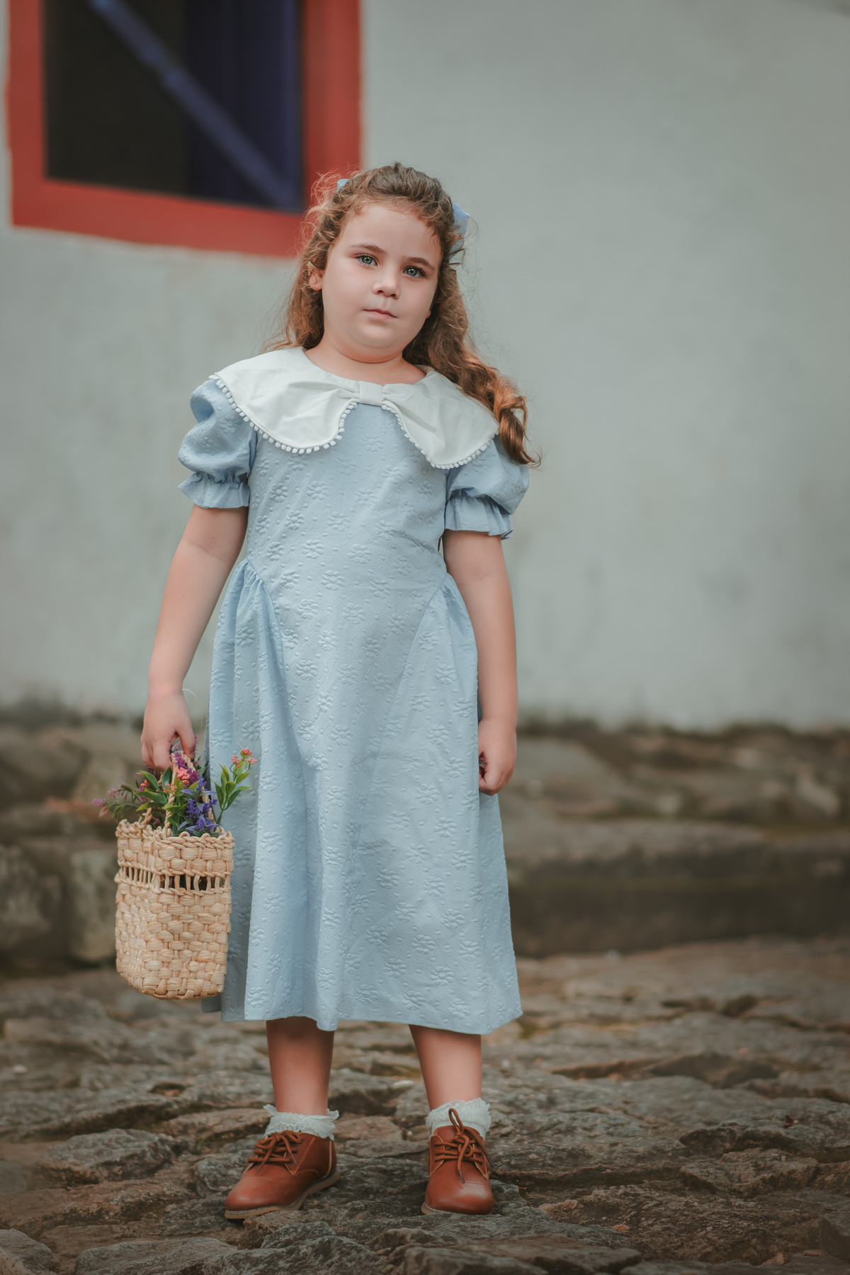 uma menina usando um vestido vintage azul e segurando uma cesta de flores durante seu ensaio fotográfico no museu de Vitória.
