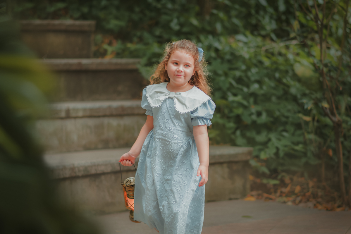 Uma menina usando vestido azul vintage e caminhando enquanto segura uma lamparina durante seu ensaio fotográfico no museu Solar Monjardim em Vitória.