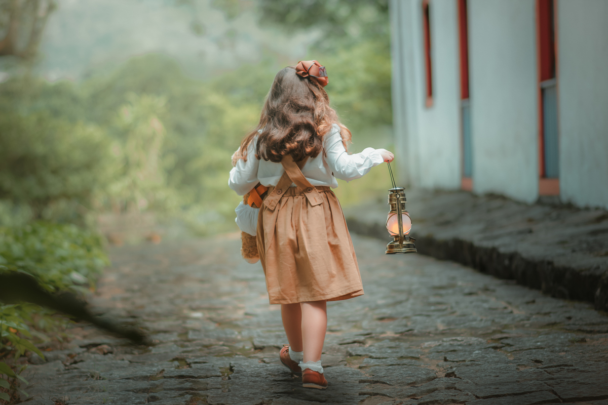 Uma menina andando em uma rua de pedras segurando uma lanterna, durante seu ensaio fotográfico.