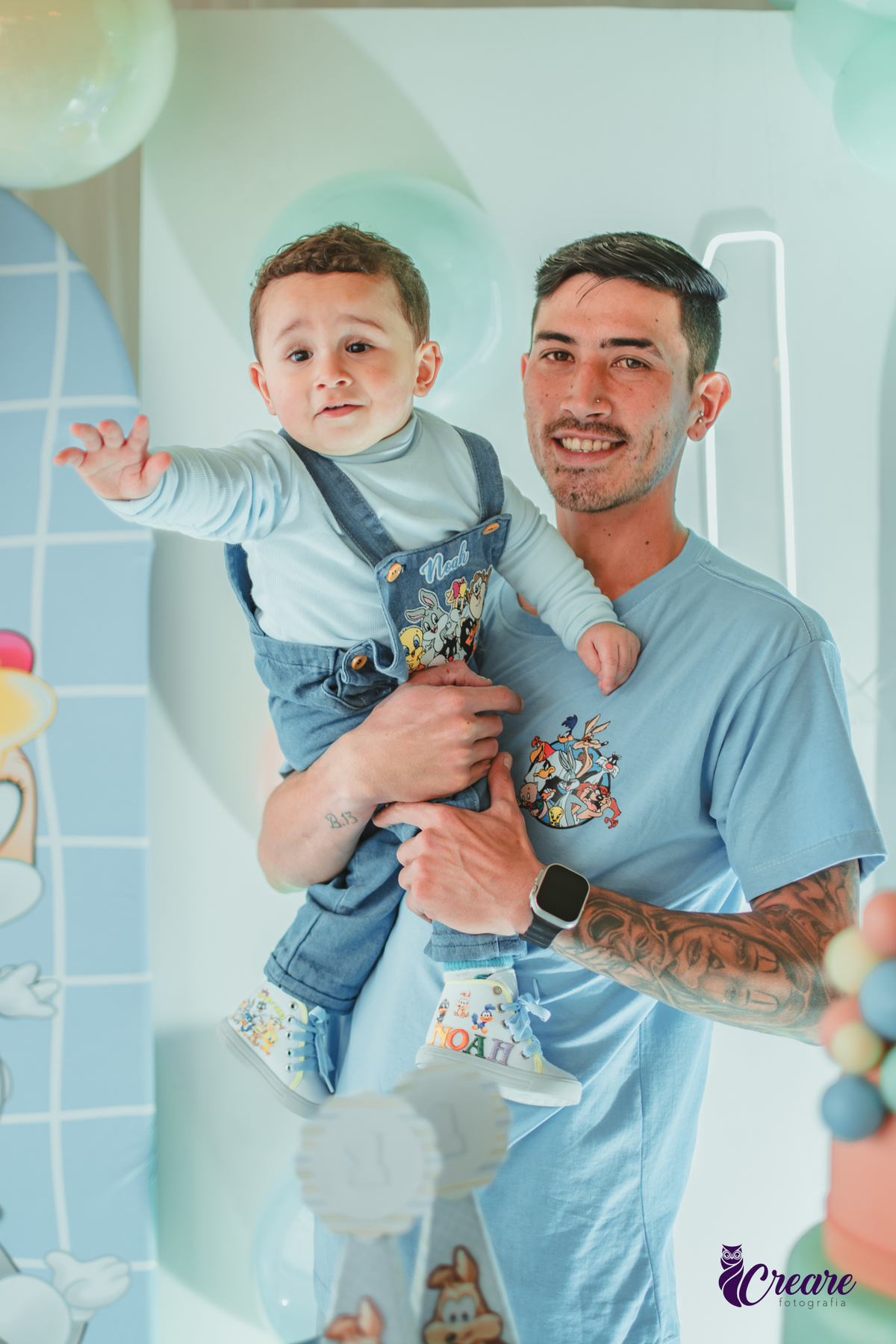 Um homem com seu filho em frente a mesa de decoração do aniversário de 1 ano.