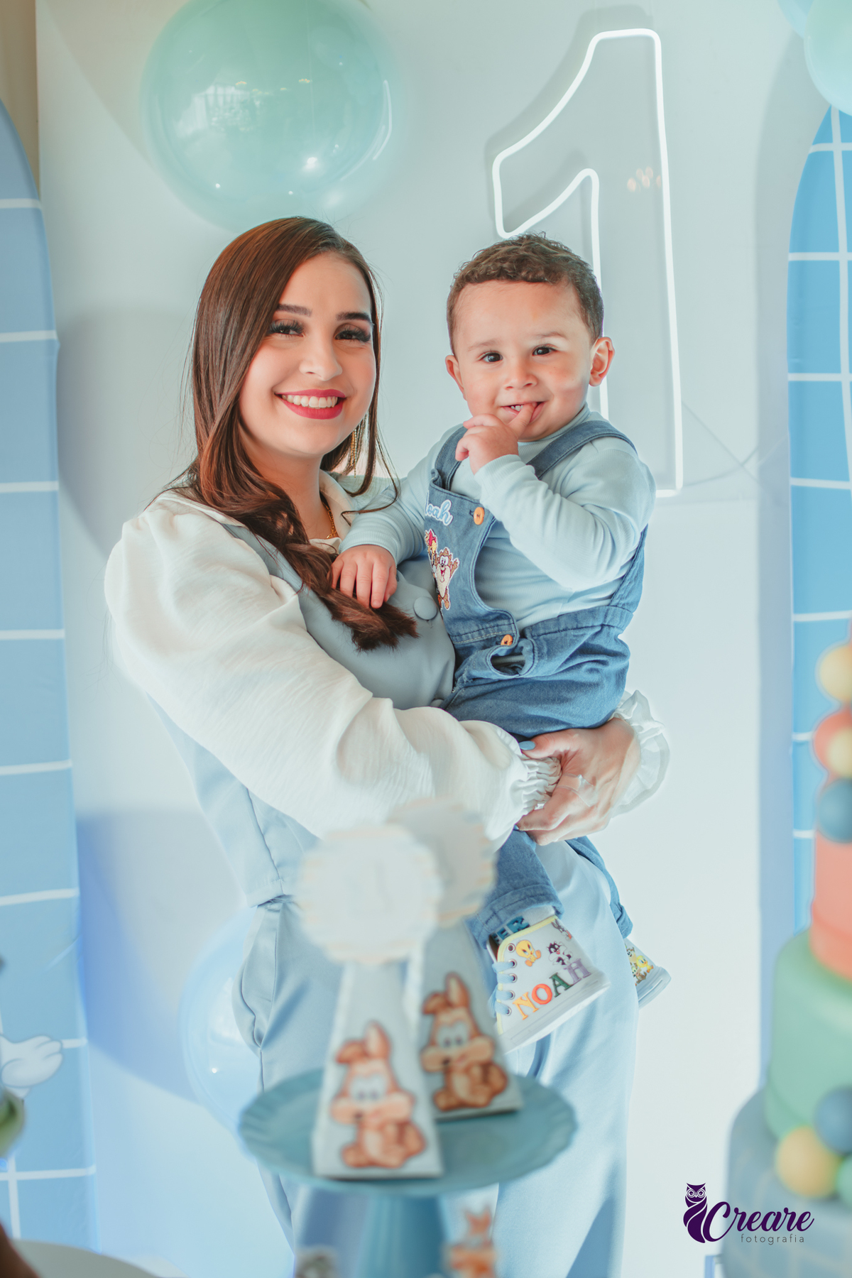 Um mãe com seu bebê em frente a mesa de decoração do aniversário de 1 ano.