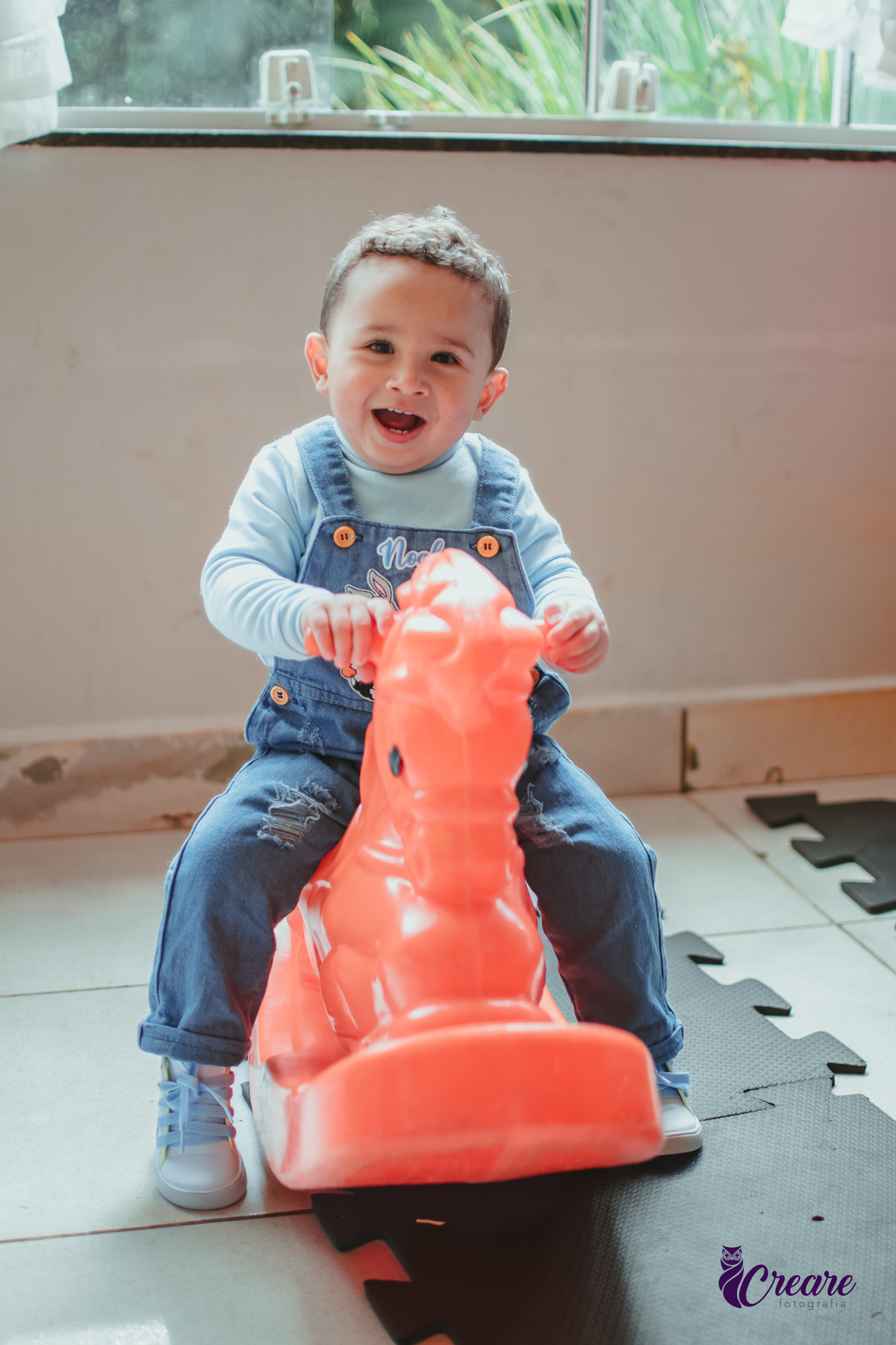 Um bebê de 1 ano brincando em um cavalinho laranja durante sua festa de aniversário.