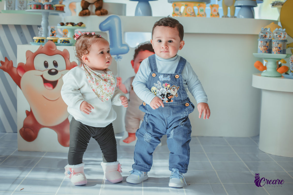 Dois bebês, um menino e uma menina, em frente uma mesa decorada com o tema Baby looney tunes em um aniversáriode 1 ano