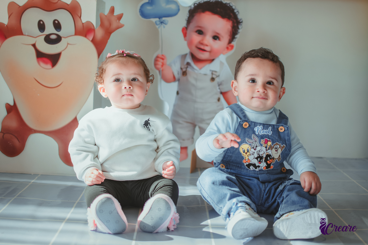 Dois bebês, um menino e uma menina, em frente uma mesa decorada com o tema Baby looney tunes em um aniversáriode 1 ano