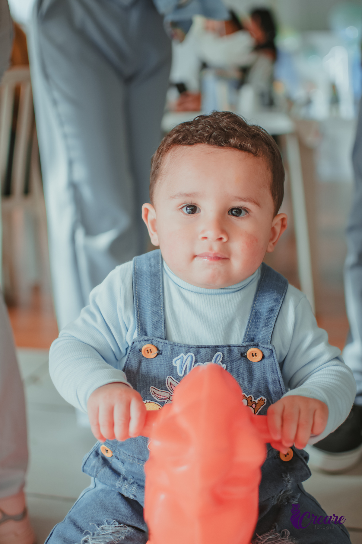 Um bebê de 1 ano brincando em um cavalinho laranja durante sua festa de aniversário.