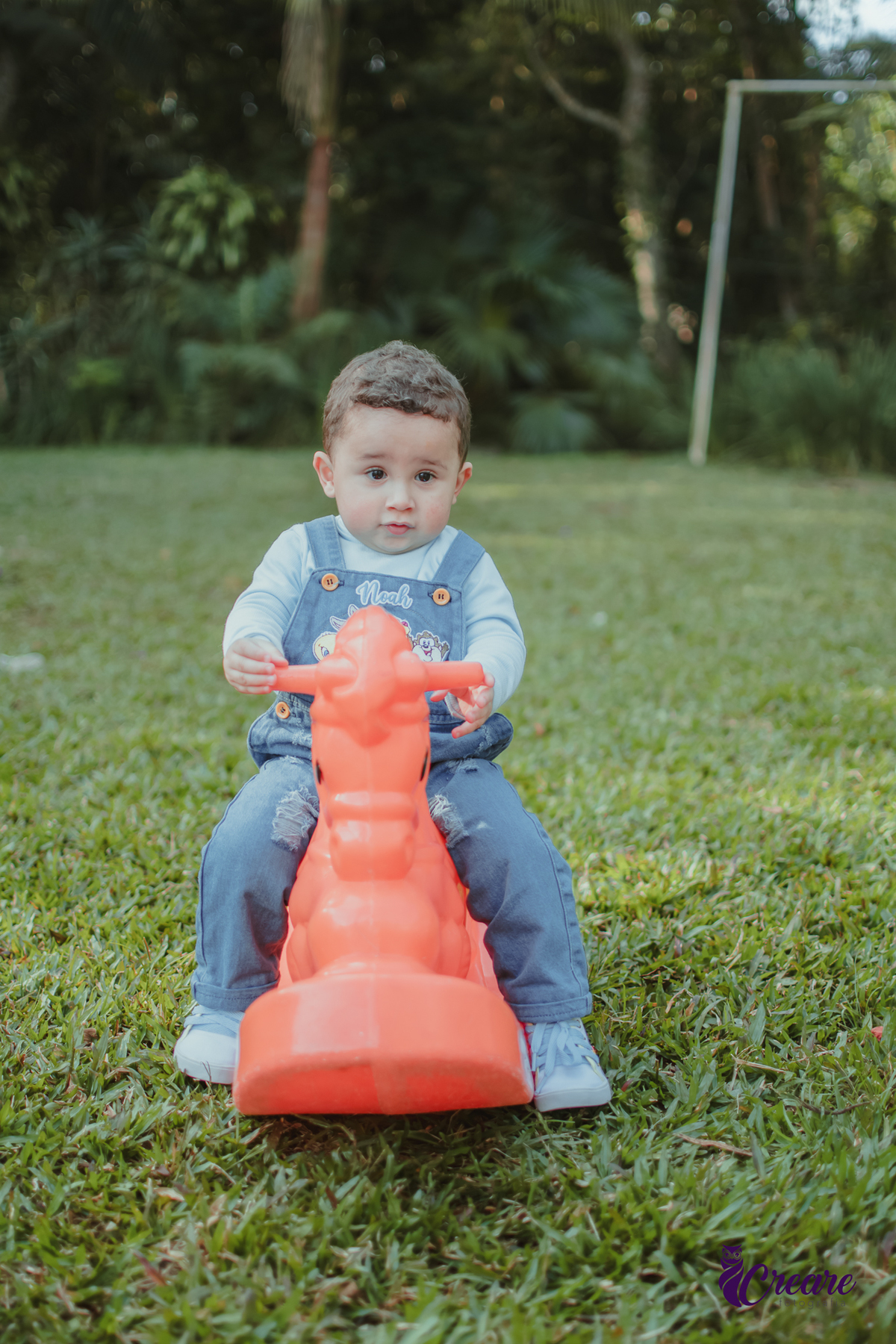 Um bebê de 1 ano brincando em um cavalinho laranja durante sua festa de aniversário.