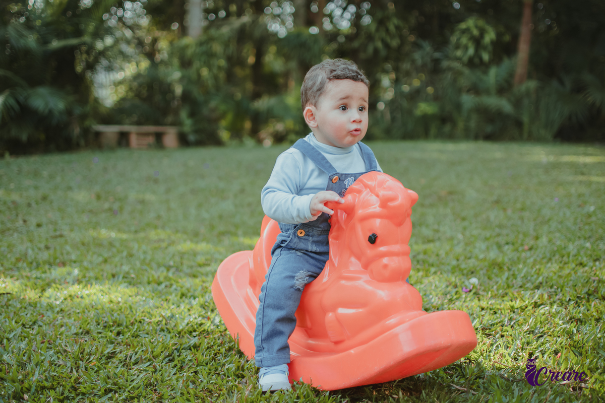 Um bebê de 1 ano brincando em um cavalinho laranja durante sua festa de aniversário.