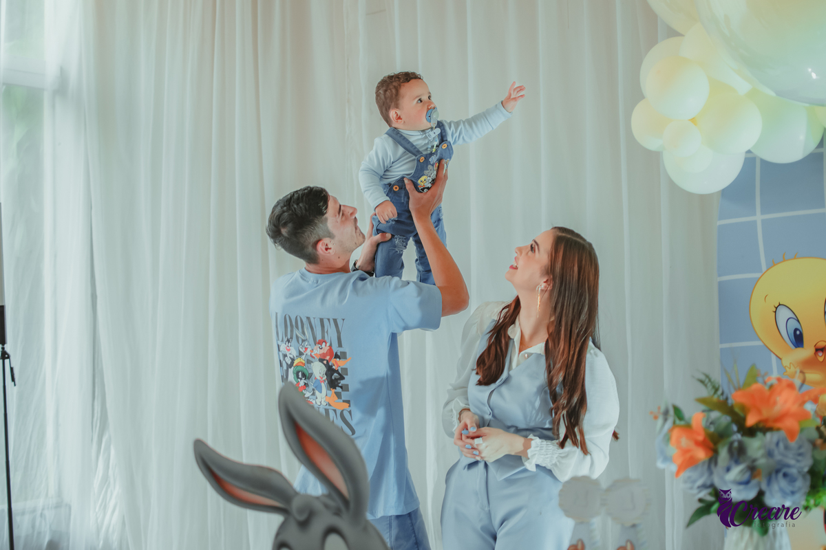 Um bebê brincando com seu pai e sua mãe, durante festa de aniversário de 1 ano.