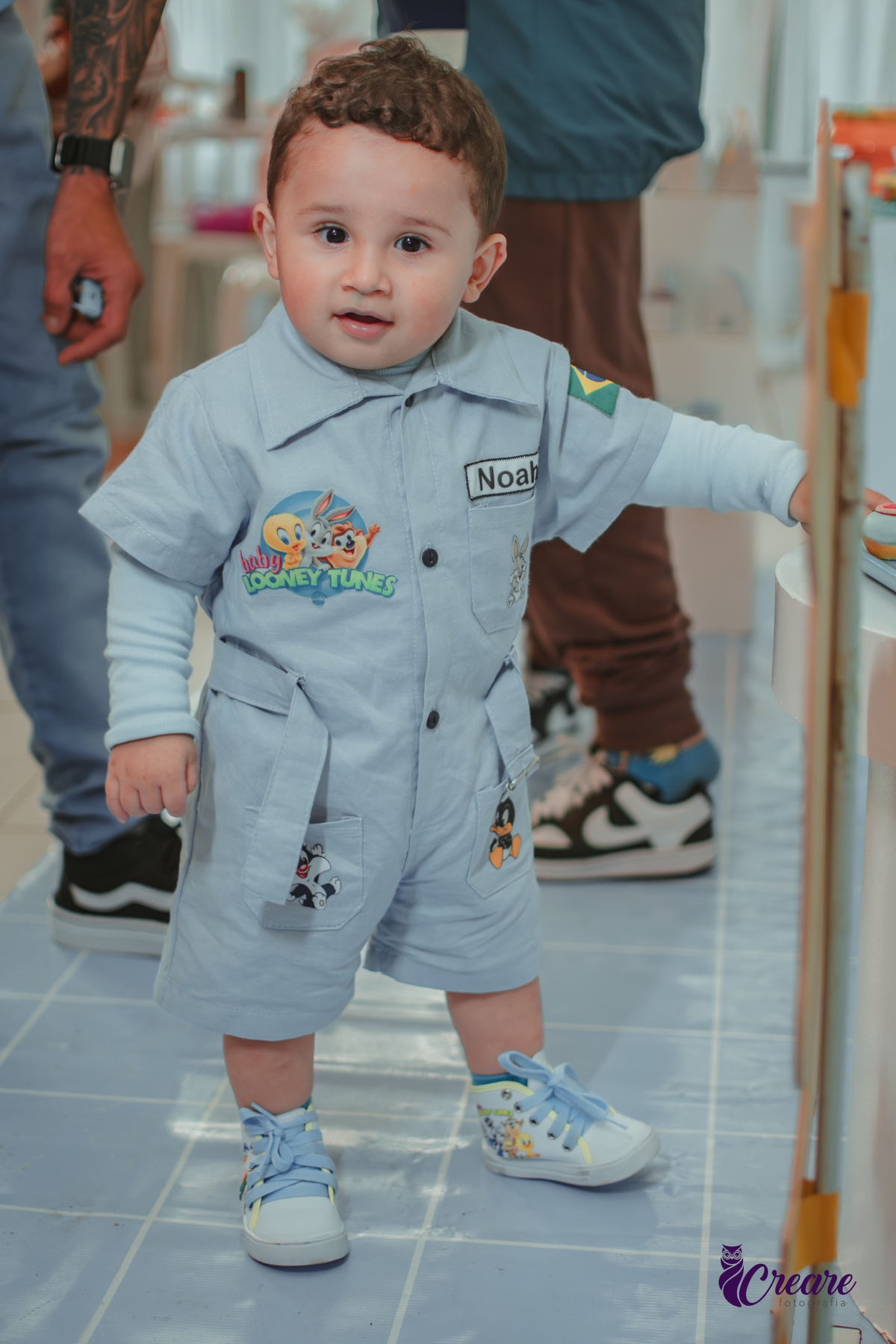 Um bebê, vestido com roupas personalizadas do desenho Baby Looney tunes e brincando em sua festa de aniversário de 1 ano.
