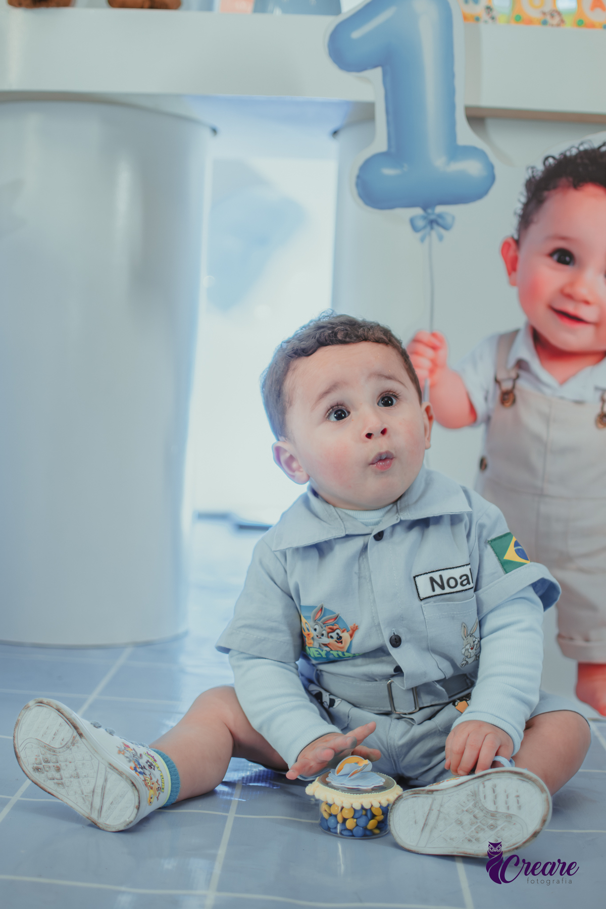 Um bebê, vestido com roupas personalizadas do desenho Baby Looney tunes e brincando em sua festa de aniversário de 1 ano.
