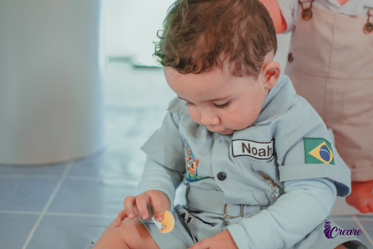 Um bebê, vestido com roupas personalizadas do desenho Baby Looney tunes e brincando em sua festa de aniversário de 1 ano.