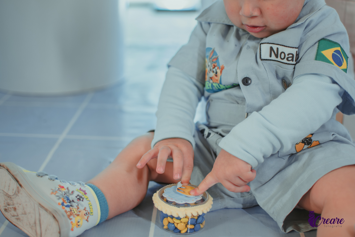 Um bebê, vestido com roupas personalizadas do desenho Baby Looney tunes e brincando em sua festa de aniversário de 1 ano.