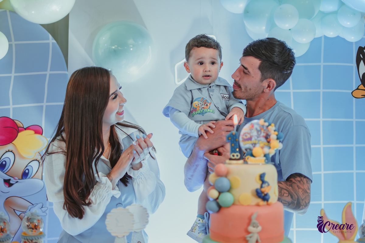 Familia com bebê de um ano, em frente a mesa de decoração do aniversário no momento do parabéns.
