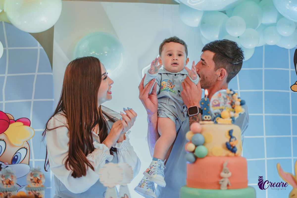 Familia com bebê de um ano, em frente a mesa de decoração do aniversário no momento do parabéns.
