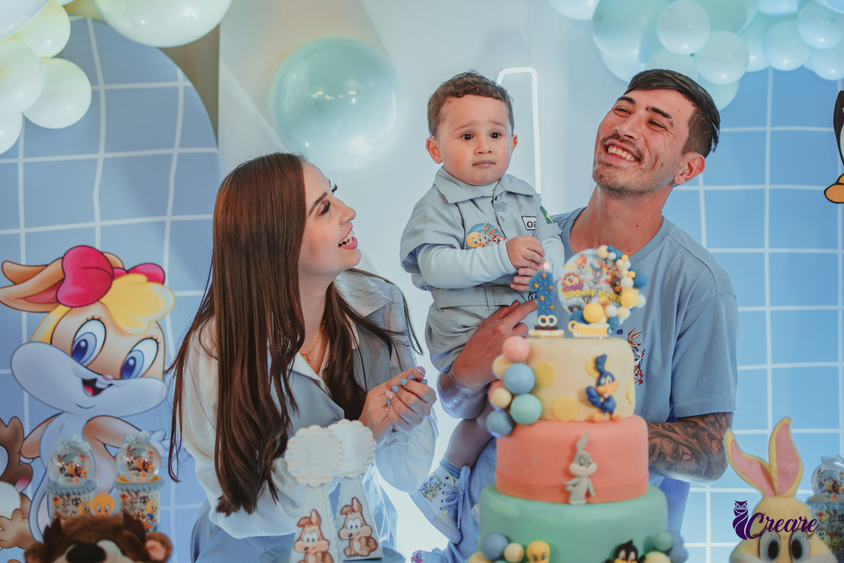 Familia com bebê de um ano, em frente a mesa de decoração do aniversário no momento do parabéns.