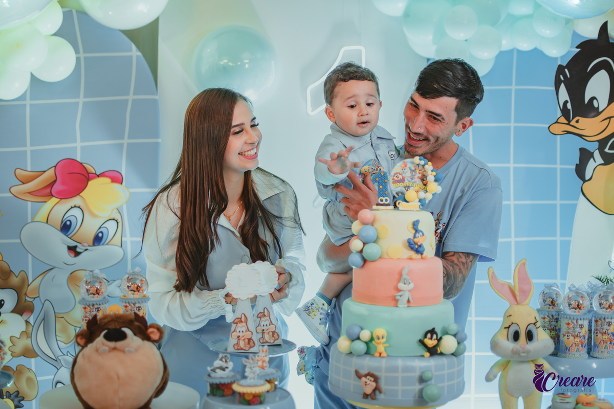 Familia com bebê de um ano, em frente a mesa de decoração do aniversário no momento do parabéns.