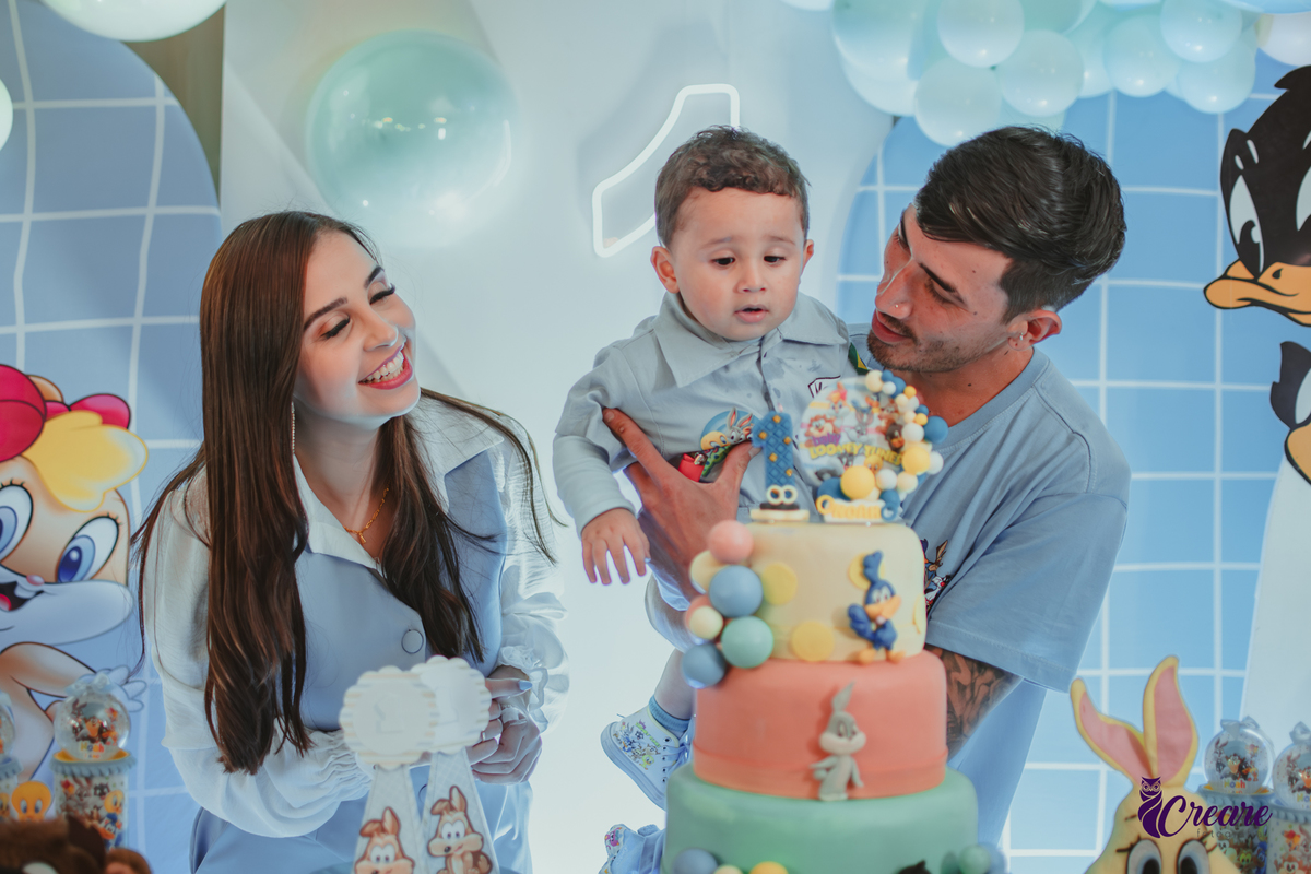 Familia com bebê de um ano, em frente a mesa de decoração do aniversário no momento do parabéns.