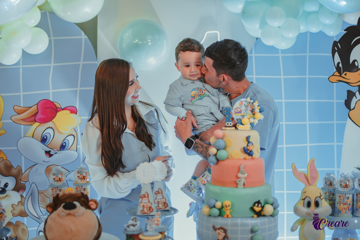 Familia com bebê de um ano, em frente a mesa de decoração do aniversário no momento do parabéns.